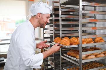 Smiling baker holding tray with fresh cooked croissants in bakehouse