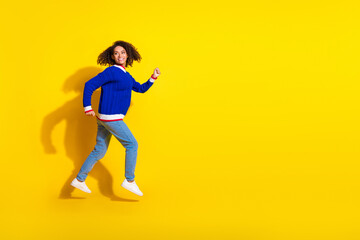 Fototapeta na wymiar Young woman in stylish blue sweater jumping joyfully against vibrant yellow background, full of energy and happiness
