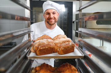 Male baker holding a tray of baked breads in bakery shop
