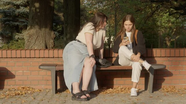 Two girlfriends of different body sizes sitting on a park bench, smiling and talking. One is slim, the other plus-size. A natural expression of love, friendship, and deep connection between women.