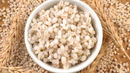 Cooked peeled barley grains in white bowl on wooden table