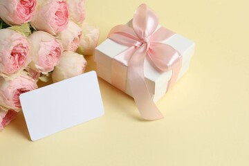 Beautiful pink peony roses with paper card and gift box on color background