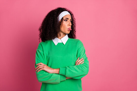 Stylish young woman in green pullover making playful face while posing against vibrant pink background