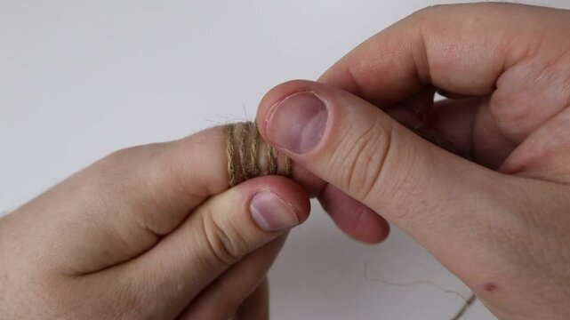 Man wraps rope around the index finger of his left hand on a white background
