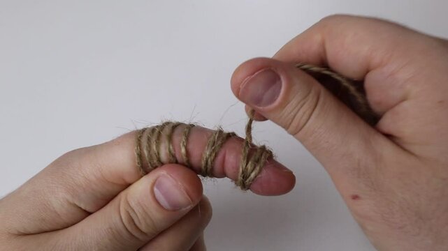 Man wraps rope around the finger of his left hand on a white background