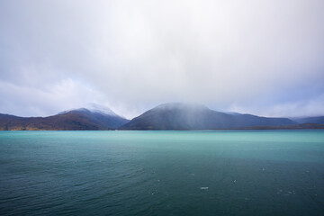 Autumn landscape of the Lyngen Alps in Northern Norway with snowy peaks, dramatic clouds, and a tranquil fjord.