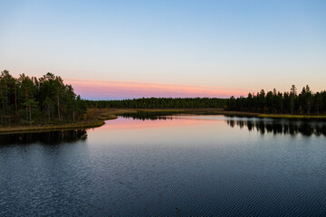 A peaceful sunset over a lake in Lapland, Sweden, with the reflection of trees in the still water.
