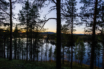A peaceful sunset over a lake in Lapland, Sweden, with the reflection of trees in the still water.
