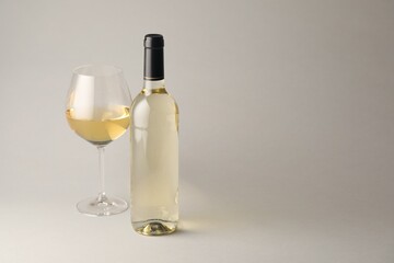 Tasty white wine in glass and bottle on light grey background, space for text