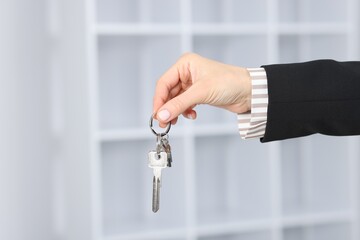 Real estate agent holding key with house shaped keychain indoors, closeup