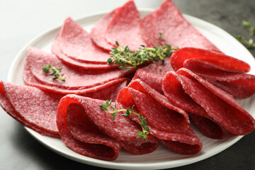 Slices of delicious sausage with thyme served on grey table, closeup