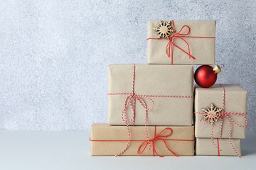Many gift boxes wrapped in kraft paper and Christmas decor on light table. Space for text