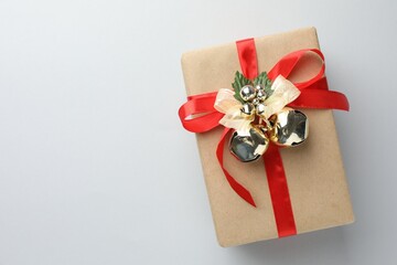 Gift wrapped in kraft paper with Christmas bells on light background, top view. Space for text