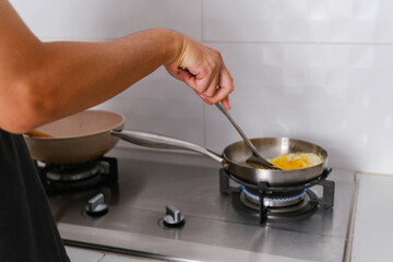 Man cooking fried egg in a frying pan on the stove. 
