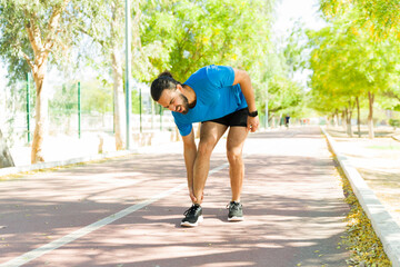 Young male runner suffering from ankle injury while training outdoors