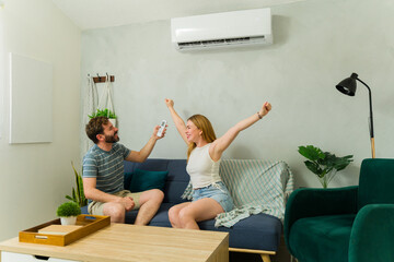 Excited couple feeling comfortable at home using air conditioning unit
