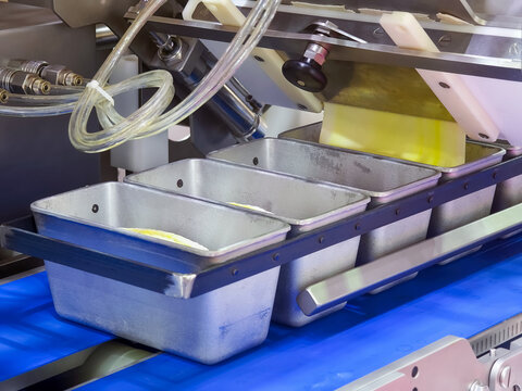 Production line processes batter filling into metal baking pans at a food manufacturing facility in the morning hours