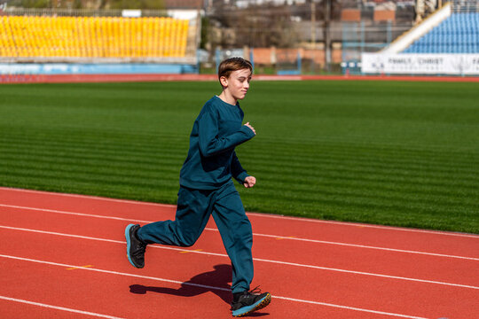 Child running on stadium. Kid exercising in athletics. Young athlete in race competition. Healthy outdoor sport for kids. Children run. Young teen boy running on the running track at stadium outdoors