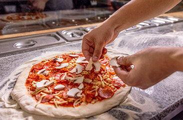 Cook in the kitchen putting the ingredients on the pizza. Man prepares pizza. Cook hand makes a...