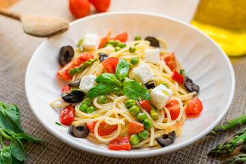Pasta primavera spaghetti close up with cherry tomatoes, black olives, feta cheese and basil, served on wooden table, with natutal light, italian dish and cuisine homemade