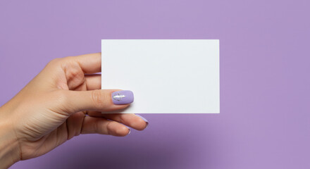 Obraz premium Hand Holding White Card: Mockup for Invitation, Greeting, or Advertisement. Purple Background, Stylish Manicure, Creative Space for Your Message