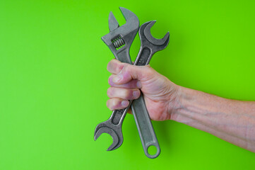 Man`s hand with adjustable wrench and spanner on green background