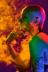 Obraz premium Side view of bald tattooed woman exhaling smoke in intense red-orange light creating mood of mystery and confidence. Concept of beauty, fashion, style, equality, makeup, wellness.
