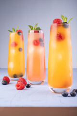 vibrant orange refreshing beverages in tall glasses with mixed berries and mint leaves on a light wooden surface under soft lighting, elegant, fancy, cocktail, contemporary, daylight, sipping