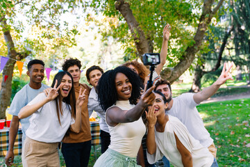 Group of cheerful young multi ethnic best friends taking a selfie at a party in the park using an action camera and a gimbal