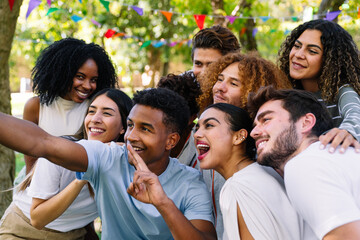 Group of cheerful multi ethnic young students taking a selfie together outdoors, making peace sign, during a college party