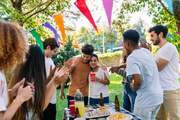Group of cheerful multi ethnic friends clapping and celebrating a young couple embracing at an...