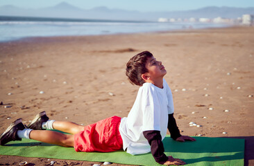 Young boy practicing cobra pose on beach yoga mat