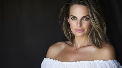 A woman with brown hair and brown eyes is wearing a white dress. She is standing in front of a black background