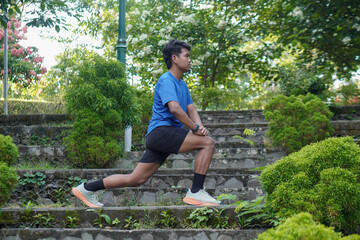 Asian man stretching his legs before a morning run in a city park, preparing for exercise with an...