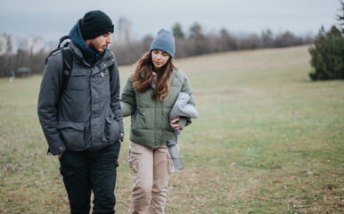 Two individuals enjoying a walk in a grassy, open landscape during an overcast day, dressed warmly for cooler weather.