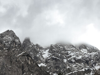 snow-covered mountains in fog. rocky peaks under a gray cloudy sky. dramatic winter landscape. untouched nature beauty. monochromatic background