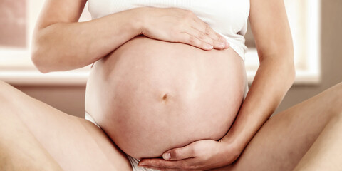 Close-up of pregnant woman's hands gently placed on her baby bump, expressing maternal love. Tender...