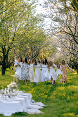 Women in white dresses are standing in a field holding hands