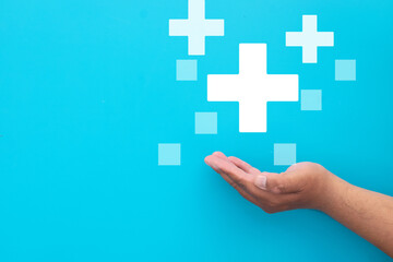 Open hand holding medical cross or plus icon on light blue background use for  modern technology in healthcare,mental health,growth mindset,positive thinking,life insurance.