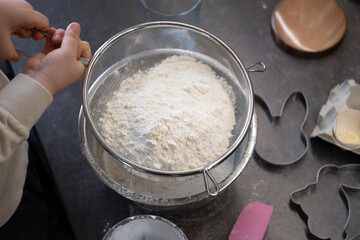 Sifting flour into bowl for Easter cookies with child helping