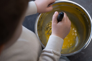 Child mixing eggs and sugar in metal bowl, baking preparation scene top view
