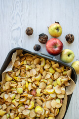 Top view of a black baking tray filled with chopped apples, fresh apples and whole walnuts on the...