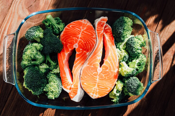 Fresh salmon and broccoli prepare for healthy cooking in a clear dish on a wooden surface