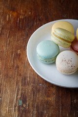 Tender multicolored macaroons with different tastes on white plate, wooden old table background, top view closeup shot