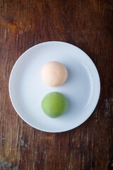 Two pink and green traditional japanese mochi or asian wagashi, rice cakes. Tasty sweets, dessert on wooden brown background. Top view, copy space