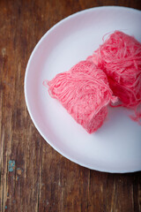 Pismaniye, cotton candy or dragons beard with berries taste on white plate, wooden background. Turkish dessert, light halva, candy floss. Top view, copy space