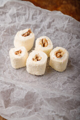 Turkish delight, white locum roll with walnut and coconut flakes on white paper, wooden background. Eastern sweets, oriental food. Traditional dessert