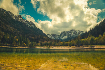 A tranquil scene from Kranjska Gora, Slovenia, featuring a crystal clear turquoise lake in the foreground.