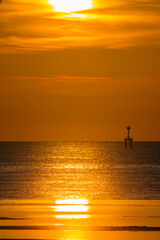A breathtaking view of the sun setting over the ocean, casting a golden glow across the sky and reflecting on the water. A lighthouse stands in the distance, adding depth to the serene coastal scene