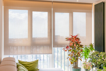 Automatic roller blinds cover large windows in a bright modern room, softly diffusing natural...